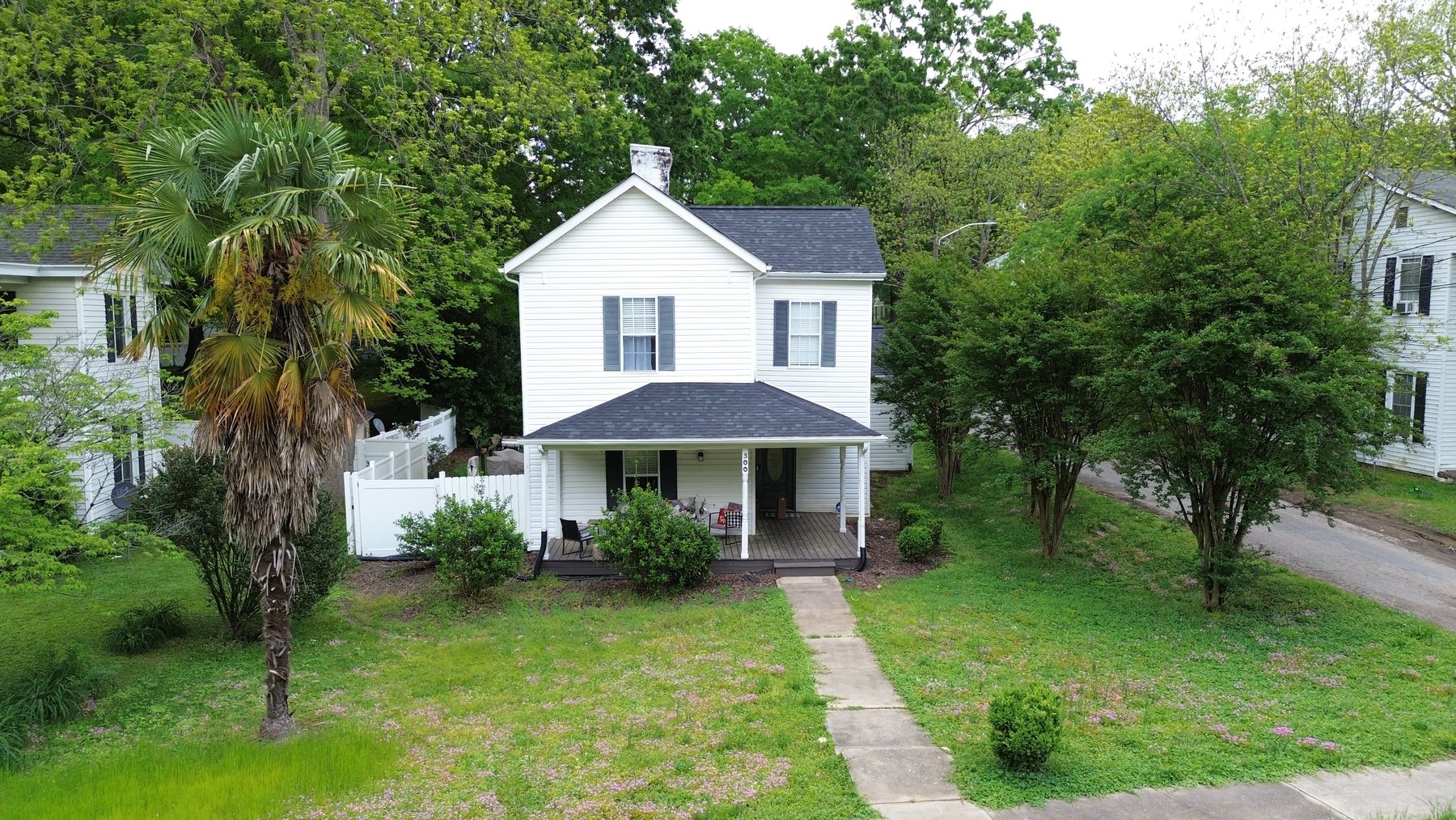 Elevated front view of a white two-story cottage with covered porch and mature landscaping